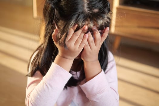 a upset child girl cover her face with hand .