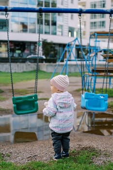 Little girl stands near the swing and looks away. Back view. High quality photo