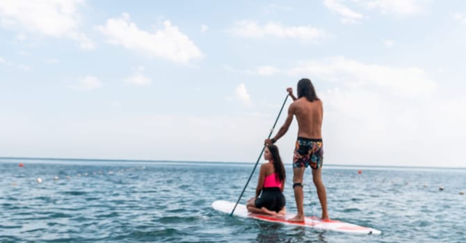 Sea woman and man on sup. Silhouette of happy young woman and man, surfing on SUP board, confident paddling through water surface. Idyllic sunset. Active lifestyle at sea or river