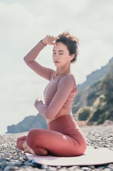 Young woman with long hair in white swimsuit and boho style braclets practicing outdoors on yoga mat by the sea on a sunset. Women's yoga fitness routine. Healthy lifestyle, harmony and meditation