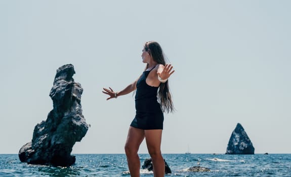 Woman travel sea. Young Happy woman in a long red dress posing on a beach near the sea on background of volcanic rocks, like in Iceland, sharing travel adventure journey