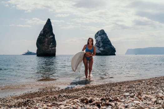 Close up shot of beautiful young caucasian woman with black hair and freckles looking at camera and smiling. Cute woman portrait in a pink bikini posing on a volcanic rock high above the sea