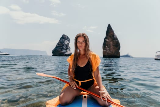 Close up shot of beautiful young caucasian woman with black hair and freckles looking at camera and smiling. Cute woman portrait in a pink bikini posing on a volcanic rock high above the sea