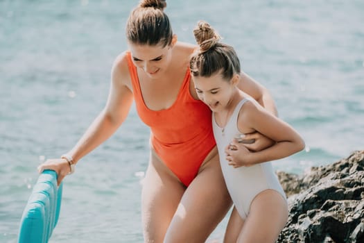 Woman and her daughter together on rock in the sea.