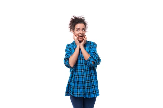 young beautiful european woman with curly hair is dressed in a blue plaid shirt with a surprised grimace on a white background.