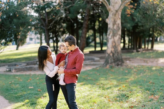 Smiling mom looking at little girl in dad arms in park. High quality photo