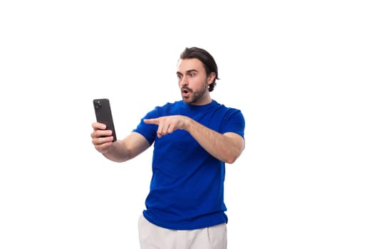 young brutal caucasian brunette man with a beard in a blue t-shirt communicates via video link on a smartphone.