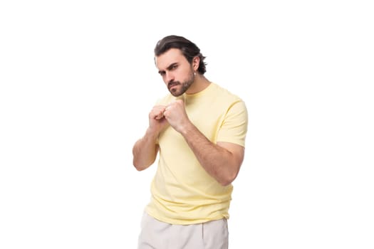 young well-groomed european brunette guy with a beard and mustache holds his fists in front of him.