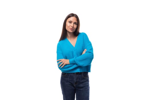portrait of a young slender brunette woman with light make-up dressed in a blue cardigan on a white background.