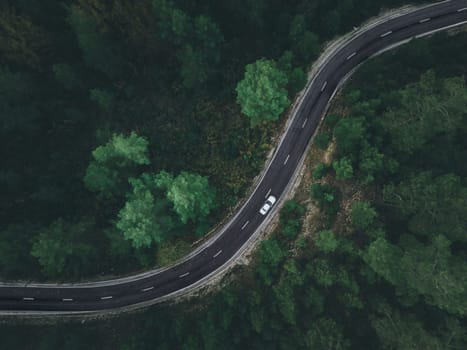 Aerial view taken by drone of a car driving on a forest road in autumn