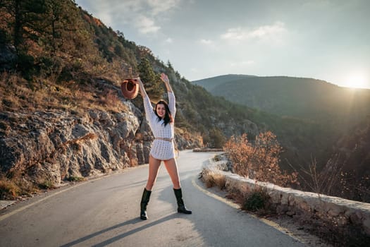 Woman road mountain. A woman in a white sweater, black boots and a hat walks along a winding alpine path between the mountains at sunset in late summer. The concept of travel