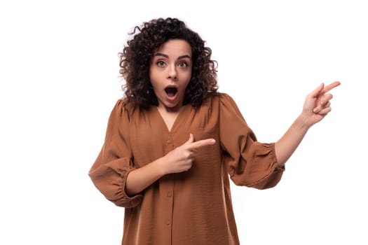 young surprised caucasian curly brunette woman dressed in a stylish brown blouse on a white background.
