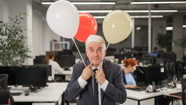 Portrait of a cheerful mature business man holding balloons in the office