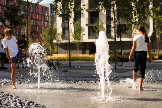Cheerful young teen girl in city fountain, girl in wet clothes is having fun and enjoying the cool summer water, background city architecture. High quality photo