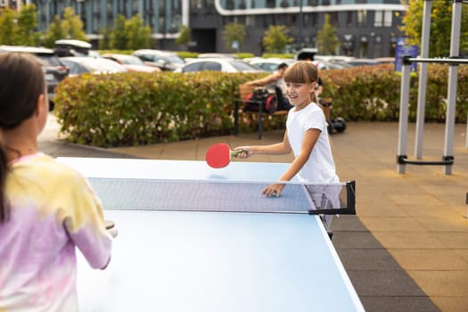 Kid playing table tennis outdoor with family. High quality photo