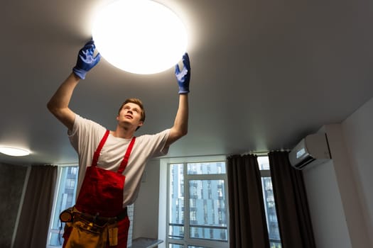 Worker installing lamp on stretch ceiling indoors