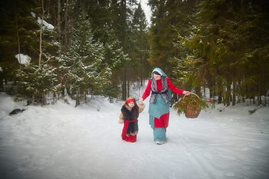 Family with mother and little daughter in stylized medieval peasant clothing in winter forest. The woman and child pose for fairy tale photoshoot in nature on a cold day. Concept of love, friendship