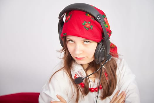 Portrait of young girl in a bright red scarf and large headphones with a microphone. A woman who is radio or television presenter in the workplace. Funny female telecom operator. Freelancer at work