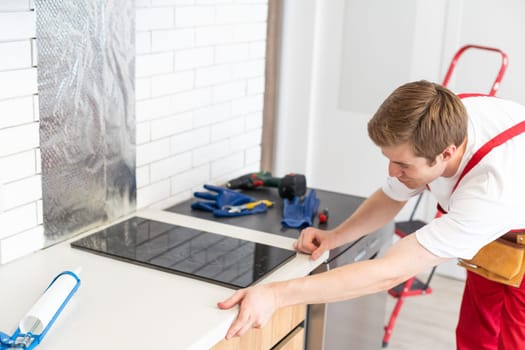 Gloved craftsman installs hob in kitchen. Household Appliance Installation Services Concept.