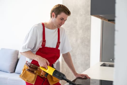 Close-up of man from professional cleaning service clean kitchen furniture with vacuum cleaner. Handyman prepare room after renovation. Cleanliness and household concept