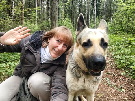 Adult girl with shepherd dog taking selfies in forest. Middle aged woman and big shepherd dog on nature. Friendship, love, communication, fun, hugs