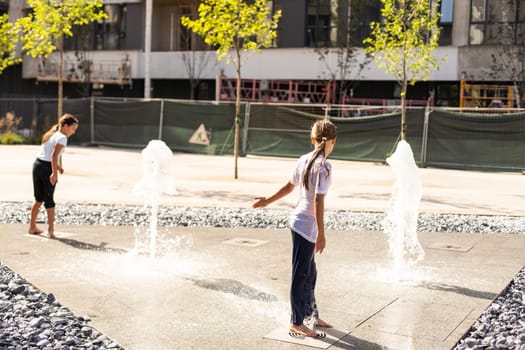 Happy teenage girl dancing in a fountain in a city park on a hot summer day. High quality photo