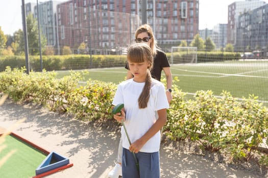 Mother and her little daughter practicing to hit the ball at the course. High quality photo