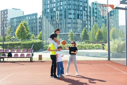 summer holidays, sport and people concept - happy family with ball playing on basketball playground. High quality photo