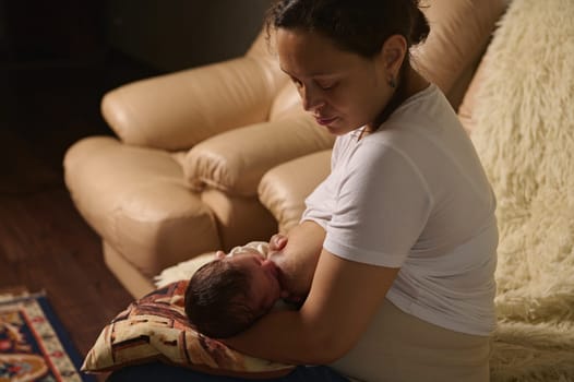 Happy serene woman, new mom sitting on the sofa at home, holding and feeding her newborn baby with breast milk. The importance of breast milk for the healthy of children during first six month of life