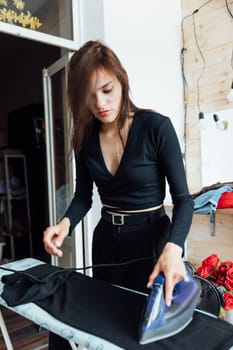 young woman ironing clothes with iron on ironing board