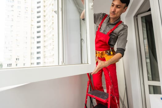 Worker in uniform installing roller window blind indoors. High quality photo