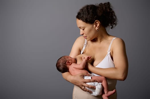 African American pretty woman, loving caring new mother in underwear, holding her newborn child, breastfeeding her baby, isolated gray background. Copy advertising space.
