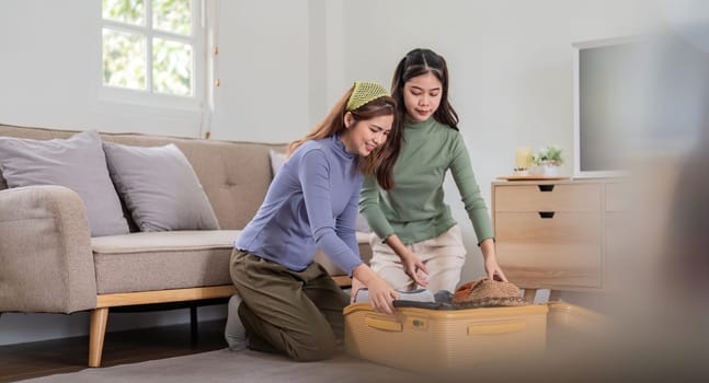 Asian woman prepare to pack clothes travel places with her friends. Asian beautiful two women friend pack things in your travel bag for holidays for her vacation trip.