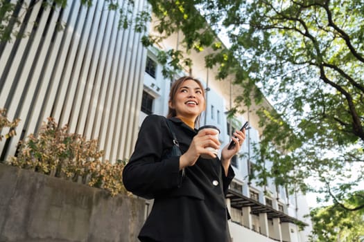 Beautiful young woman Using smartphone standing on the city street along with drinking coffee. portrait of gorgeous Smiling female using mobile phone.