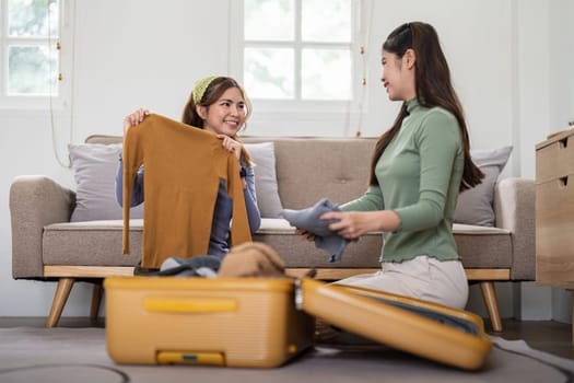 Asian woman prepare to pack clothes travel places with her friends. Asian beautiful two women friend pack things in your travel bag for holidays for her vacation trip.