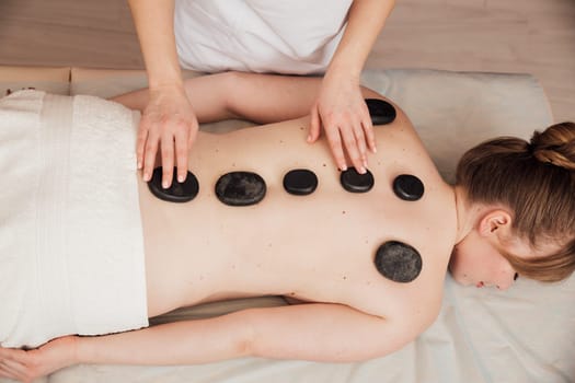 Female masseur doing back massage with stones