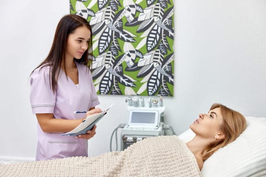 female cosmetologist talking with woman client in beauty clinic.