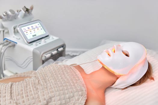 Woman lies with led light therapy facial mask in beauty salon