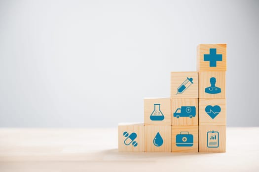 Representation of healthcare and insurance via pyramid-stacked wooden cubes. Crowning medical insurance icon suggests safety. Blue background presents copyspace for Health Insurance communication.