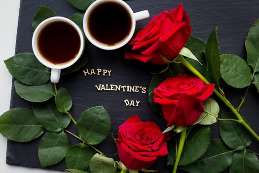 The inscription Happy Valentine on a black background with red roses and coffee
