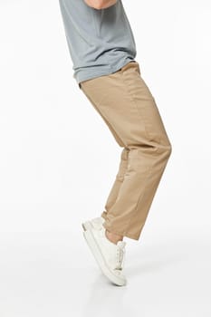 man wearing white sneakers and casual beige pants on studio background. side view