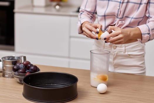 female hands breaking eggs for baking at modern kitchen