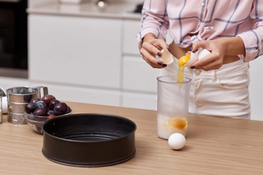 female hands blend eggs for plum pie at kitchen