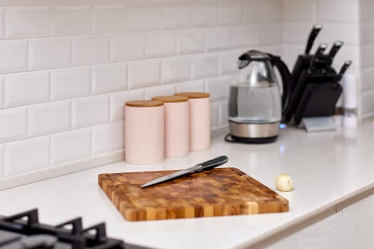 Knife and fresh piece of raw meat on wooden cutting board in modern white kitchen