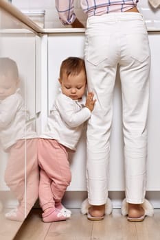 mother doing housework with her baby girl. woman cleaning dishes and kid is upset because she wants to play