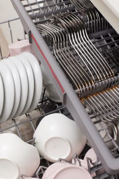 Open built-in dishwasher machine with clean cutlery, dishes, plates in white modern kitchen. top view