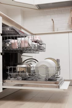 Open built-in dishwasher machine with clean cutlery, dishes, plates in white modern kitchen. side view