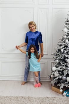 Mom and daughter at the christmas tree with gifts and toys