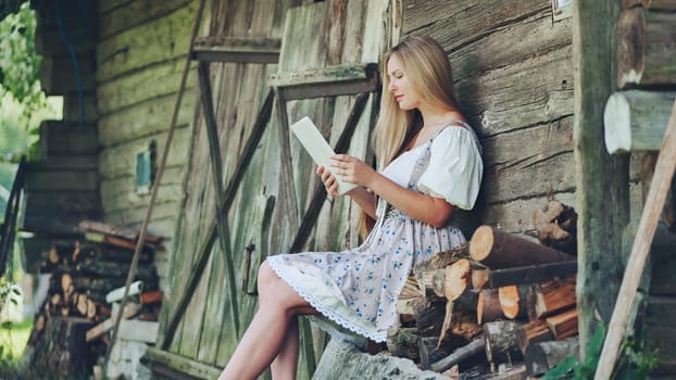 Village Slavic girl flipping a tablet in the countryside by the barn