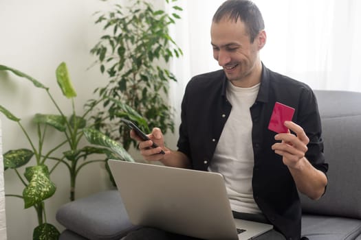 Smiling man sitting in office and pays by credit card with his mobile phone